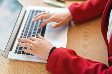 A woman in a red blazer is typing on her laptop. She's working on a project, focused on meeting her deadline.