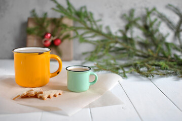 Two cups of coffee with milk on a white wooden table. Next to the Christmas shortbread cookies on craft paper. In the background is a branch of a Christmas tree and a New Year's gift.Christmas holiday