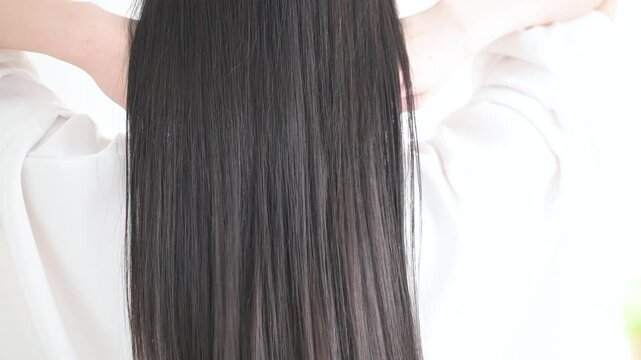 艶のあるロングヘアの黒髪の女性の後ろ姿の顔無し　キューティクルな美しいストレートヘアの揺れる髪の毛　ヘアケアなどのイメージのスロー動画