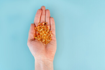 A man's hand holds omega-3 fish oil capsules on a blue table background. The concept of healthy nutrition and vitamins. Close up, point of view shot.