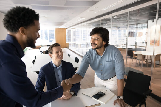 Positive Indian CEO shaking hands African client start negotiating in modern office, establish strong, trustworthy business relationships, express respect, thanking for getting professional services - Powered by Adobe