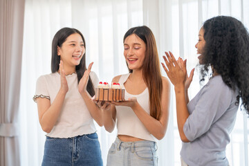 Multicultural group of women friends happy surprising friend with birthday cake at joyful party, celebration of friendship and happiness, happy birthday, candles, smiles, gift and fun at home