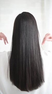 艶のあるロングヘアの黒髪の女性の後ろ姿の顔無し　キューティクルな美しいストレートヘアの揺れる髪の毛　ヘアケアなどのイメージのスロー縦動画