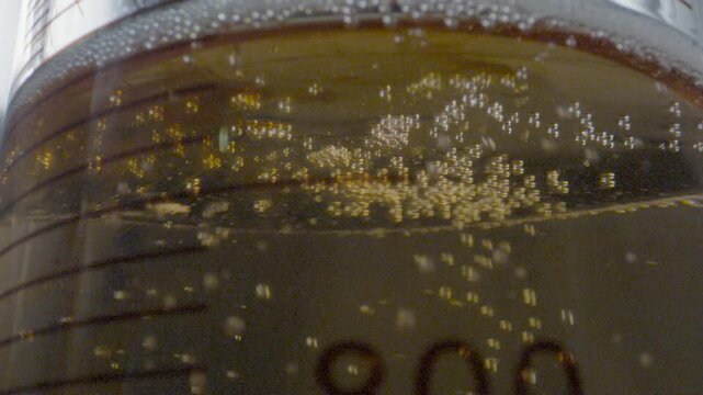 Close-up of a drop of colored liquid descending from a burette and falling into a flask with gaseous liquid in a laboratory setting.