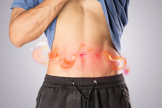 Against a gray background, a man clutches his lower back, indicating shingles pain radiating along his waistline.