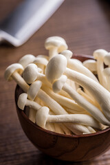 Raw white shimeji mushrooms in bowl on wooden table.