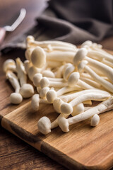 Raw white shimeji mushrooms on wooden cutting board.
