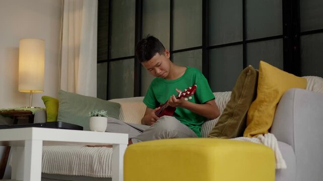 Asian boy learning to play ukulele