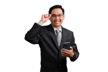 Confident young Asian businessman smiling and adjusting glasses while holding a smartphone, isolated on transparent background