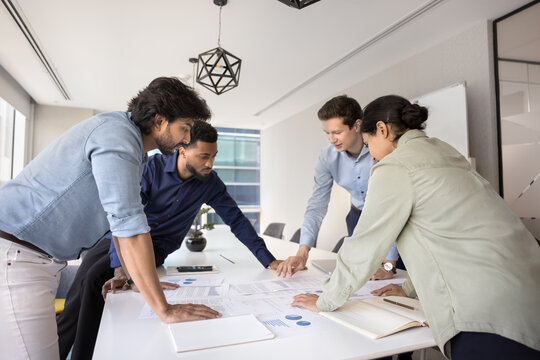 Multiethnic team reviewing financial reports, analyzing revenue and expenses gathered around conference table, discuss project progress, evaluating milestones, planning next steps, developing strategy