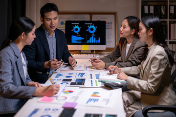 A group of people are sitting around a table with a computer monitor and papers