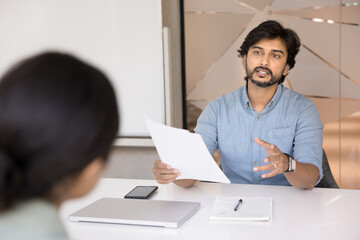 Indian HR manager interviewing female applicant in office. Financial advisor consulting bank client about mortgage or loan terms, holds legal paper document provide information, sell company services