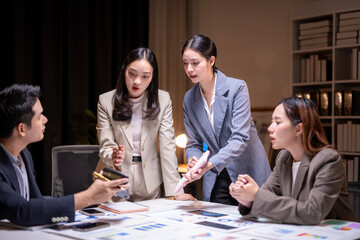 A group of people are sitting around a table with papers and a pen