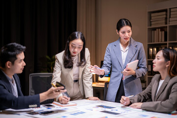A group of people are sitting around a table with a laptop and a cell phone