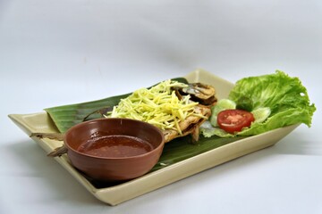 Fried star pomfret fish served with spicy mango sambal on a white plate. Traditional Indonesian seafood dish with a fresh, tangy, and savory flavor combination.