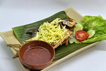 Fried star pomfret fish served with spicy mango sambal on a white plate. Traditional Indonesian seafood dish with a fresh, tangy, and savory flavor combination.