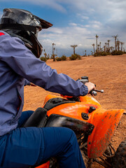 Quad adventure in the desert landscape of the Palmeraie near Marrakesh, Morocco, featuring palm trees, dry sandy terrain and a rider on an all-terrain vehicle under a partly cloudy sky.