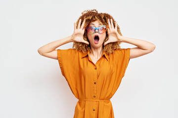 Surprised woman expressing excitement with hands on her face in a vibrant orange dress against a...