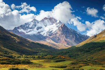 Snow capped mountain peak under a blue sky with white clouds and green valley in the foreground