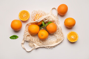 Ripe juicy oranges in cotton string bag on light gray background. Eco-friendly thread bag for shopping, buying food, fruits, vegetables. Zero waste, plastic free concept 