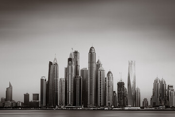 Monochrome city skyline with tall skyscrapers reflecting on calm water under a cloudy sky, Dubai Marina bay UAE