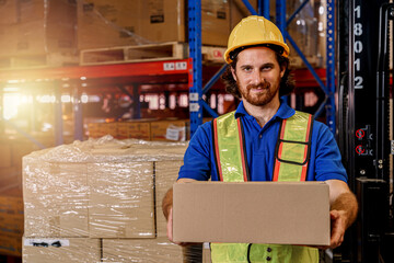 A confident warehouse worker holding a cardboard box in a storage warehouse. 