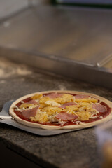 Raw Hawaiian Pizza with Ham and Pineapple on Peel Ready for Oven