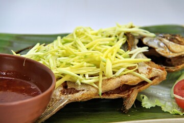 Fried star pomfret fish served with spicy mango sambal on a white plate. Traditional Indonesian seafood dish with a fresh, tangy, and savory flavor combination.