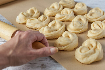 Close-up of a woman's hand with a rolling pin against a background of raw buns.