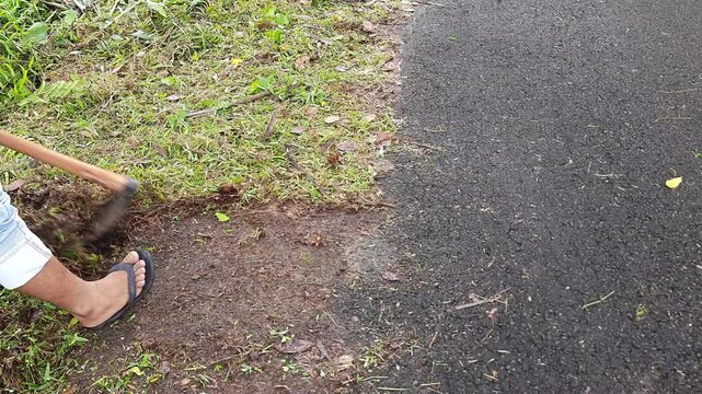 Village Worker Removing Grass Growing on Asphalt Road