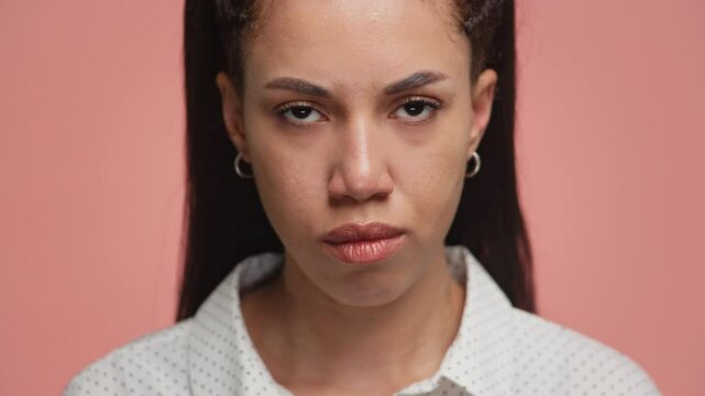 Angry woman staring intensely at camera on pink background
