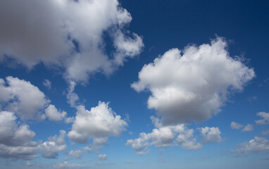 White cumulus clouds set against a blue sky with a narrow strip of land visible