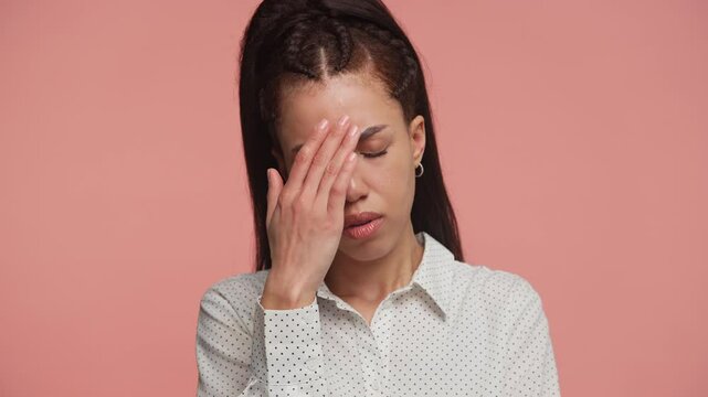 Worried young woman covering face in distress on pink background