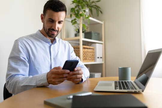 Man using phone, sending text message while working at home office. Copy space.