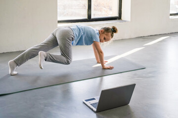 Fitness child exercises actively at home using a laptop for online workout guidance. 