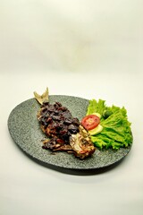 Grilled yellowtail fusilier fish with Parape sauce, a traditional Indonesian seasoning. Served on a plate with garnish, showcasing authentic seafood cuisine