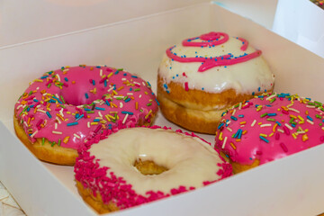 Glazed and decorated donuts in a box, showcasing a variety of flavors and toppings, with vibrant icing colors, set on a wooden table, perfect for a sweet treat or dessert
