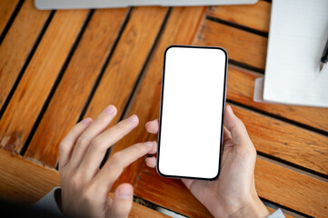 Right hands holding a white screen smartphone on wooden table with left hand hovering over.
