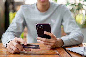 A man holding smartphone and other hand holding a credit card while sitting at wooden table.