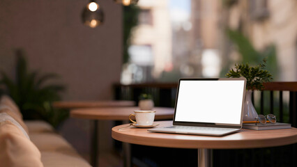 A white screen laptop and coffee cup on stool table with fabric sofa on the cafe terrace or balcony.