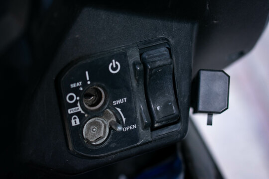 Close up of an ignition keyhole and control panel on an automatic scooter, showing the lock, seat, and power buttons