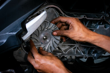 Close up of a mechanic's hands working on a scooter's CVT transmission system, focusing on the front pulley shaft during maintenance