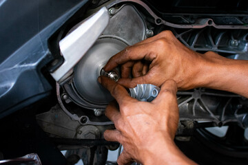 Close up of a mechanic's hands working on a scooter's CVT transmission system, focusing on the front pulley shaft during maintenance