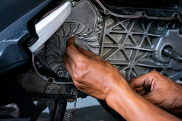 Close up of a mechanic's hands working on a scooter's CVT transmission system, focusing on the front pulley shaft during maintenance
