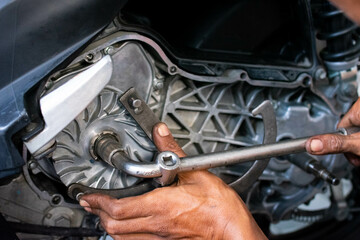 Close up of a mechanic's hands working on a scooter's CVT transmission system, focusing on the front pulley shaft during maintenance
