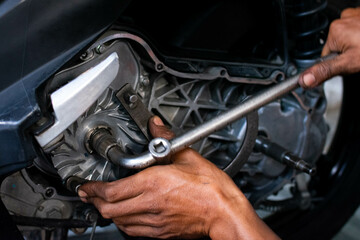Close-up of a mechanic's hands working on a scooter's CVT transmission system, focusing on the front pulley shaft during maintenance