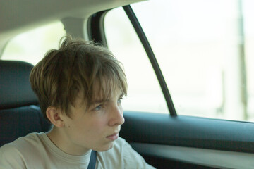 A thoughtful and introspective teenager is gazing out of a car window, completely lost in deep...