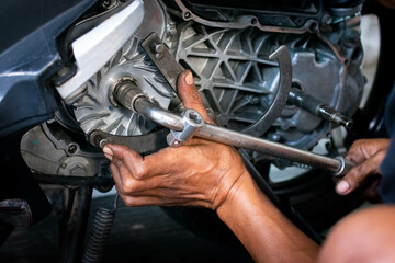 Close up of a mechanic's hands working on a scooter's CVT transmission system, focusing on the front pulley shaft during maintenance