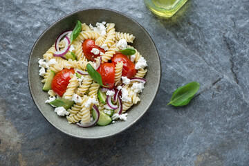 Bowl of fusilli pasta salad on a dark-grey granite background, horizontal shot with space, above view