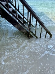 Metal stairs descend into foamy seawater, partially submerged, with gentle waves washing against...
